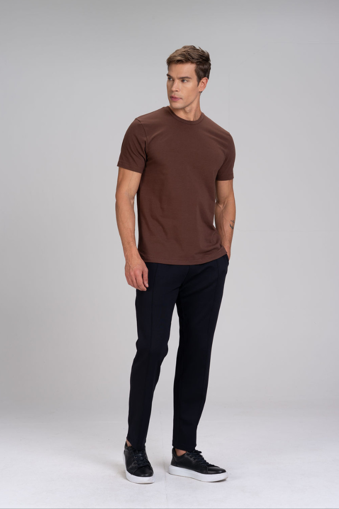 Homem de corpo inteiro vestindo camiseta masculina marrom em algodão duplo egípcio Urbô, calça escura e tênis.