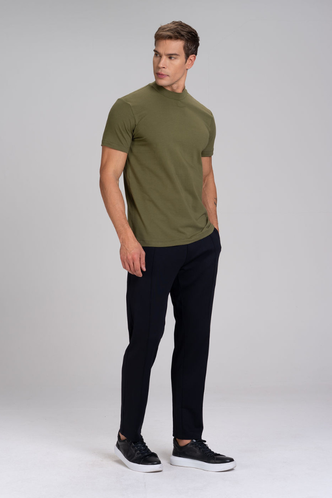Homem de corpo inteiro vestindo camiseta masculina verde gola alta em algodão duplo egípcio Urbô, calça escura e tênis.