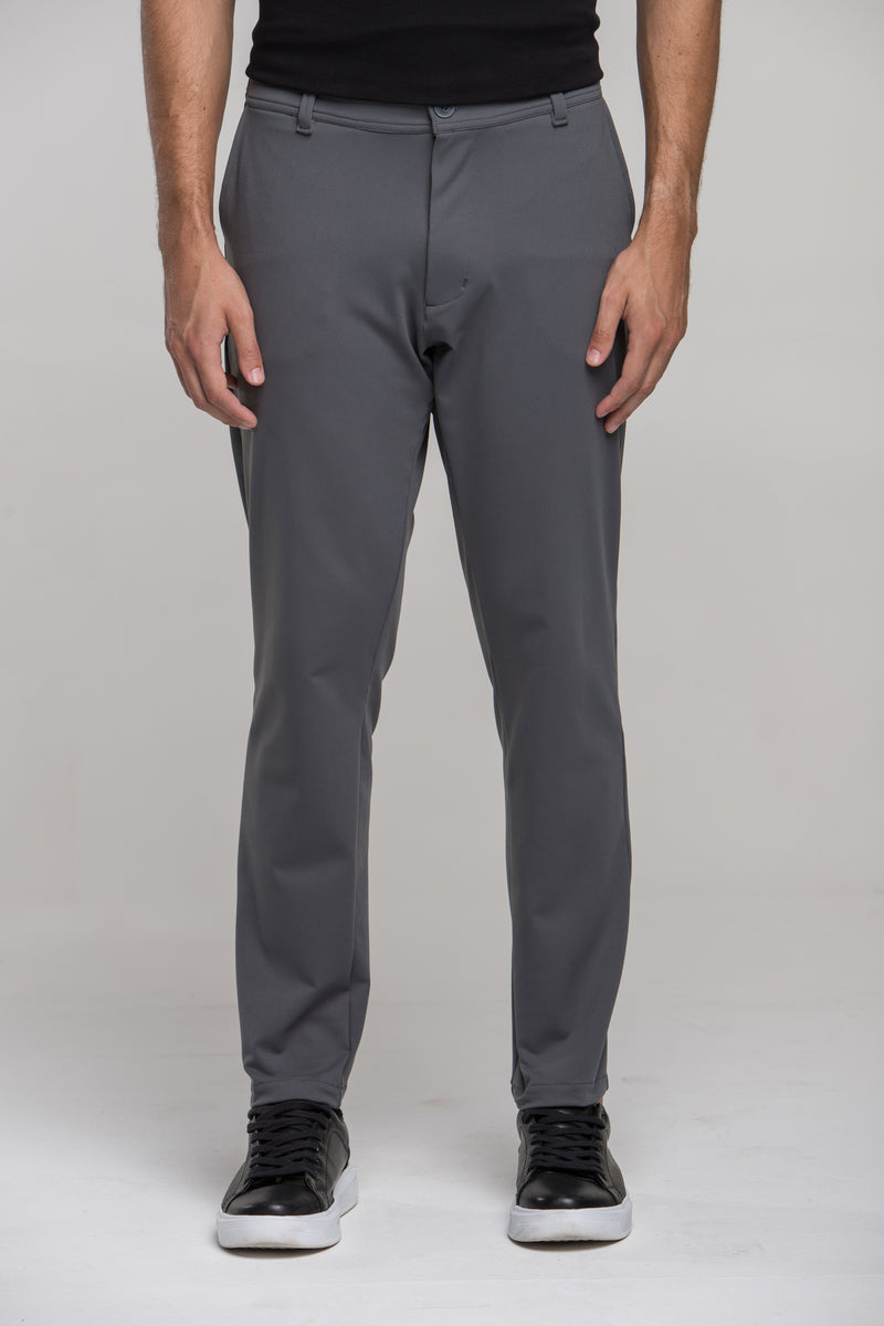 Homem de corpo inteiro vestindo calça masculina de alfaiataria tecnológica Strong cinza Urbô, camiseta preta e tênis escuro.
